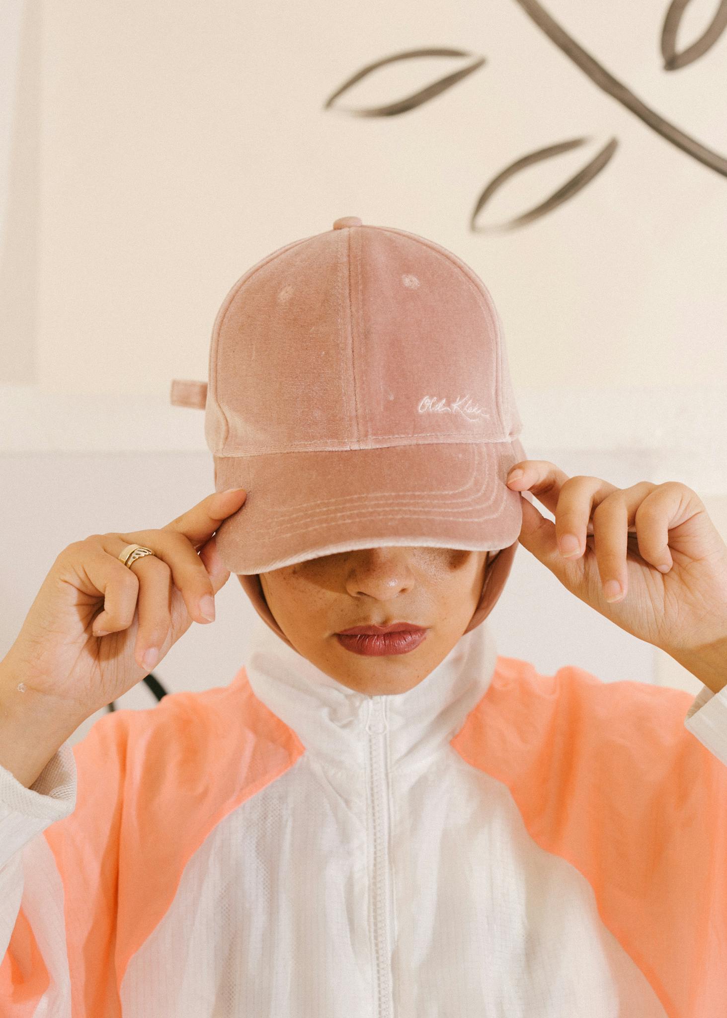Fashionable woman in pink hat and sporty outfit, holding the cap's brim.