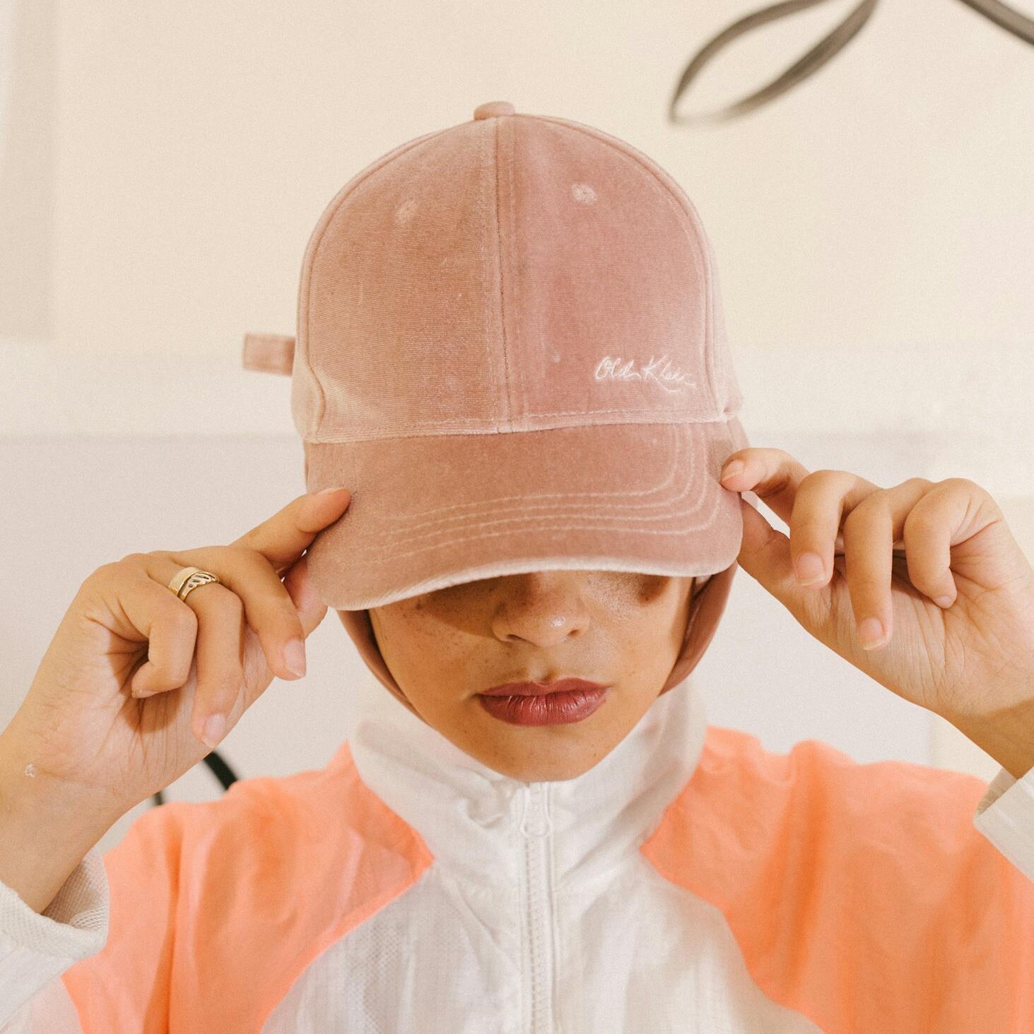 Fashionable woman in pink hat and sporty outfit, holding the cap's brim.